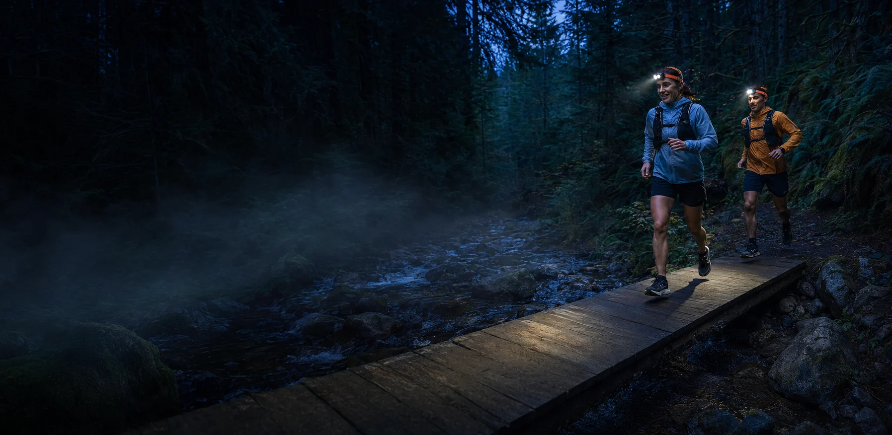 Two runners wearing HM65R-T V2 headlamps across a forest creek bridge